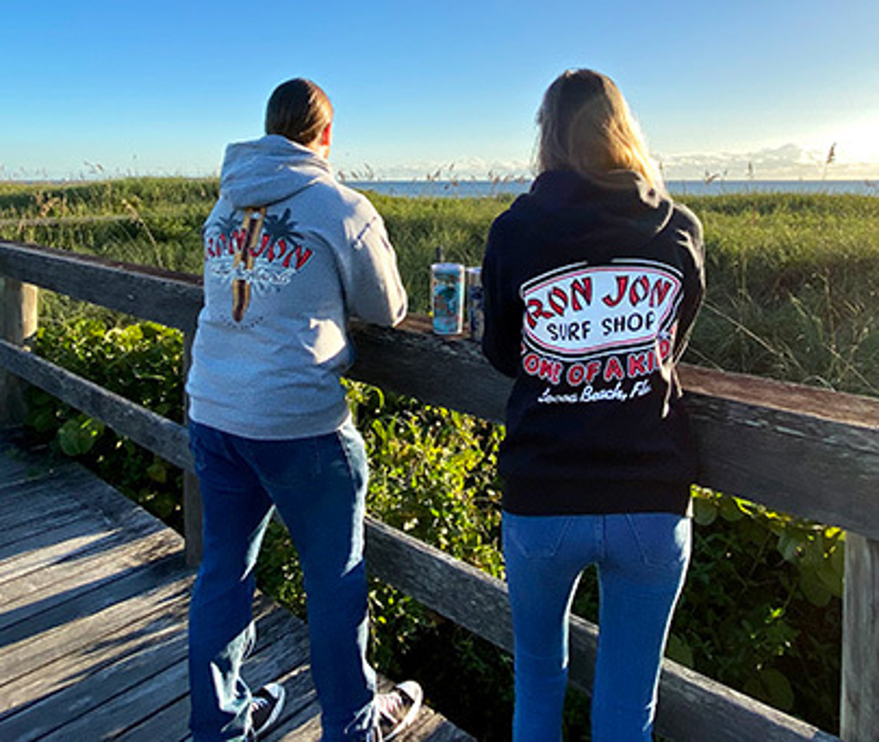 guy and girl standing on a boardwalk wearing ron jon hoodies